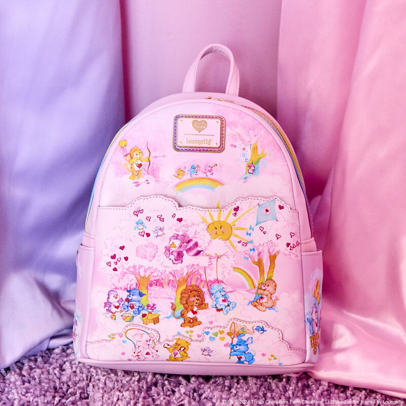 Loungefly Care Bears Cousins mini backpack featuring various Care Bears and Cousins characters playing together against a colorful, cloudy background on a pastel pink mini backpack. The backpack sits against a pink and purple background. 